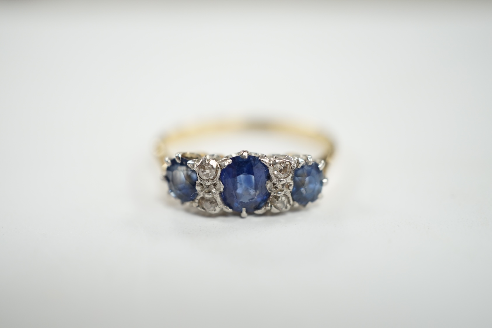 An 18ct and plat. three stone sapphire and four stone diamond chip spacer set ring, size N/O, gross weight 3.2 grams. Condition - poor to fair